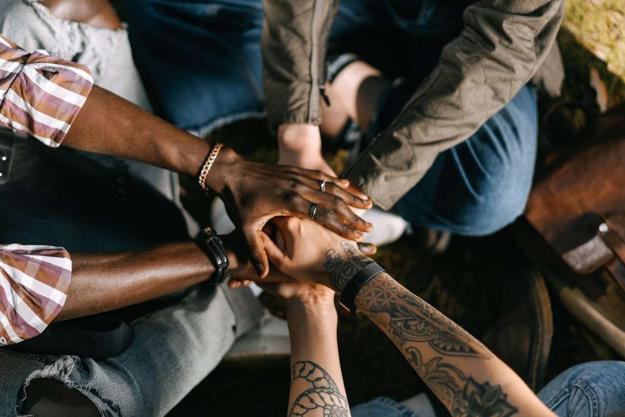 A top-down close-up shot of a diverse group of professionals stacking their hands together in a circle, demonstrating teamwork, corporate unity, and mutual support.