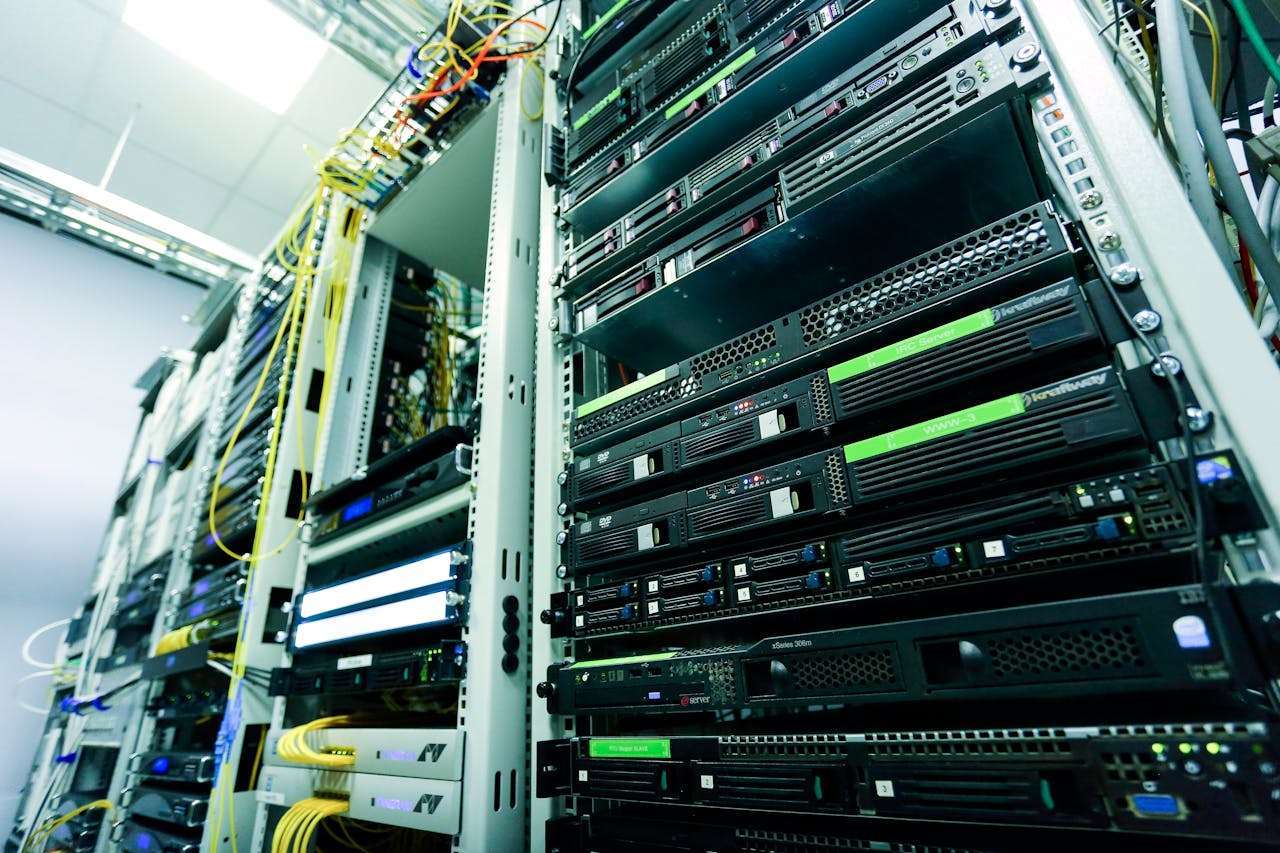 A low-angle wide shot of rows of technical data center server enclosures filled with blinking network switches, blades, and structured yellow fiber optic cabling bundles.